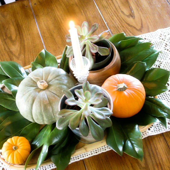 fall centerpiece with succulents, magnolia leaves, pumpkins, and candles