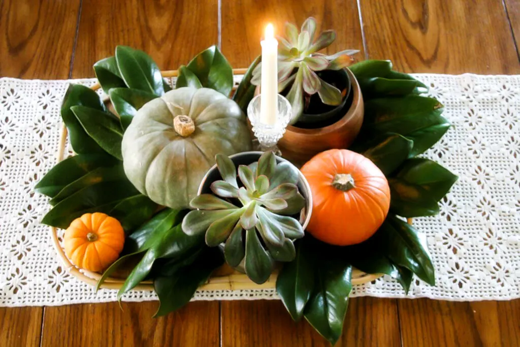 fall centerpiece with succulents, magnolia leaves, pumpkins, and candles