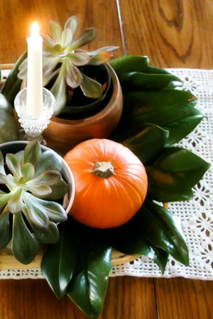 thanksgiving centerpiece with succulents, magnolia leaves, pumpkins, and candles