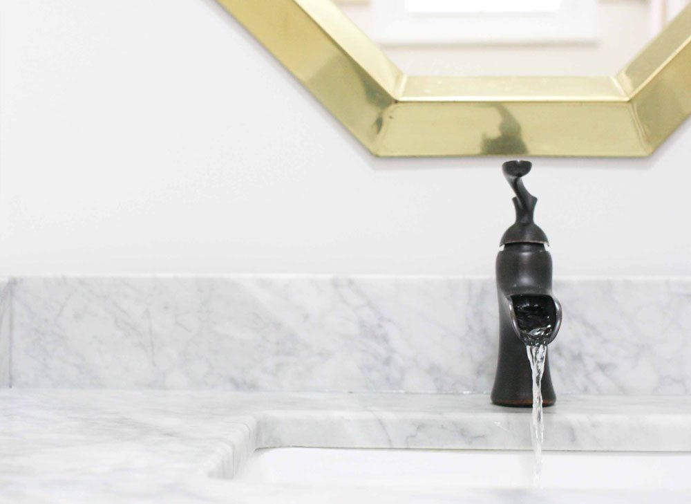 Marble counter tops with a black faucet and brass mirror that were used for a bathroom vanity makeover.