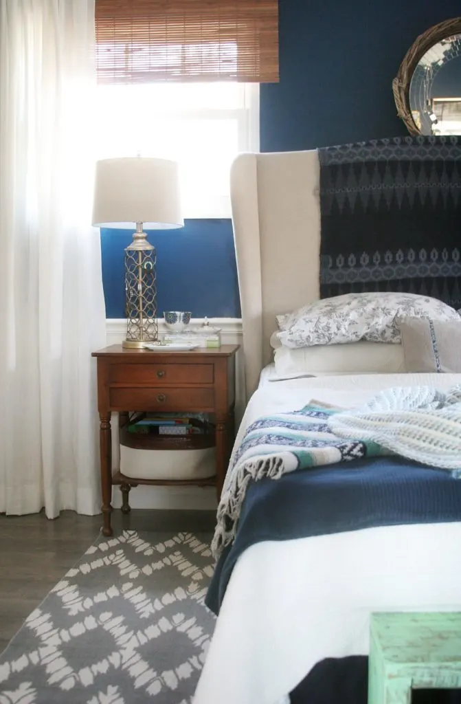 Master Bedroom Makeover // grey rug, navy walls, white curtains, white bedding, upholstered headboard, wood floors, small night stand, gold lamp, bamboo shades // Light & Bright Eclectic Home Tour by @CraftivityD