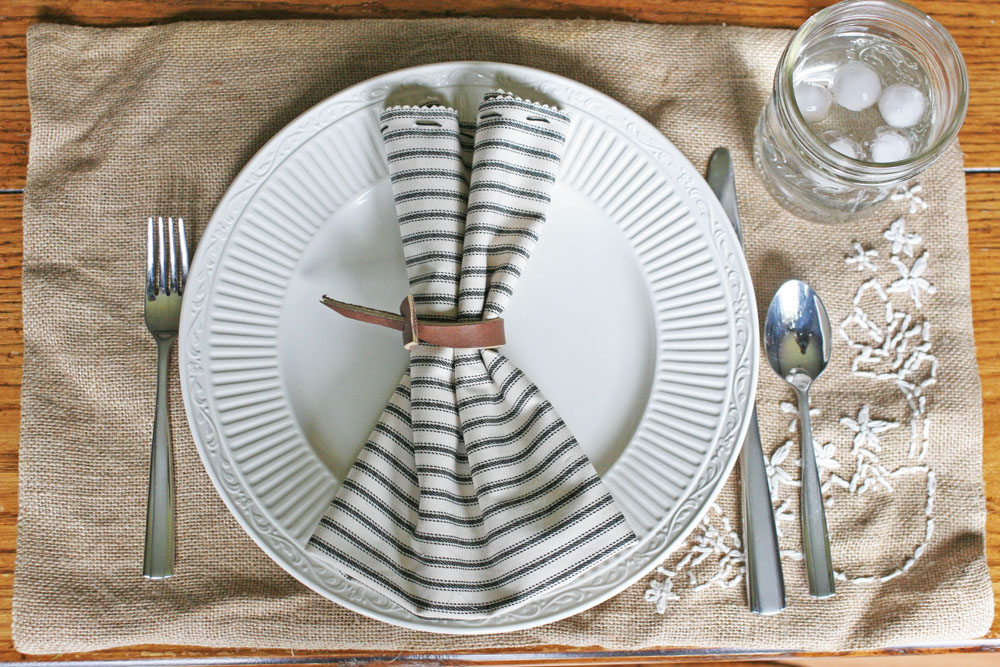 casual place setting with leather diy napkin ring, ticking cloth napkin, mason jar glass, burlap placemat
