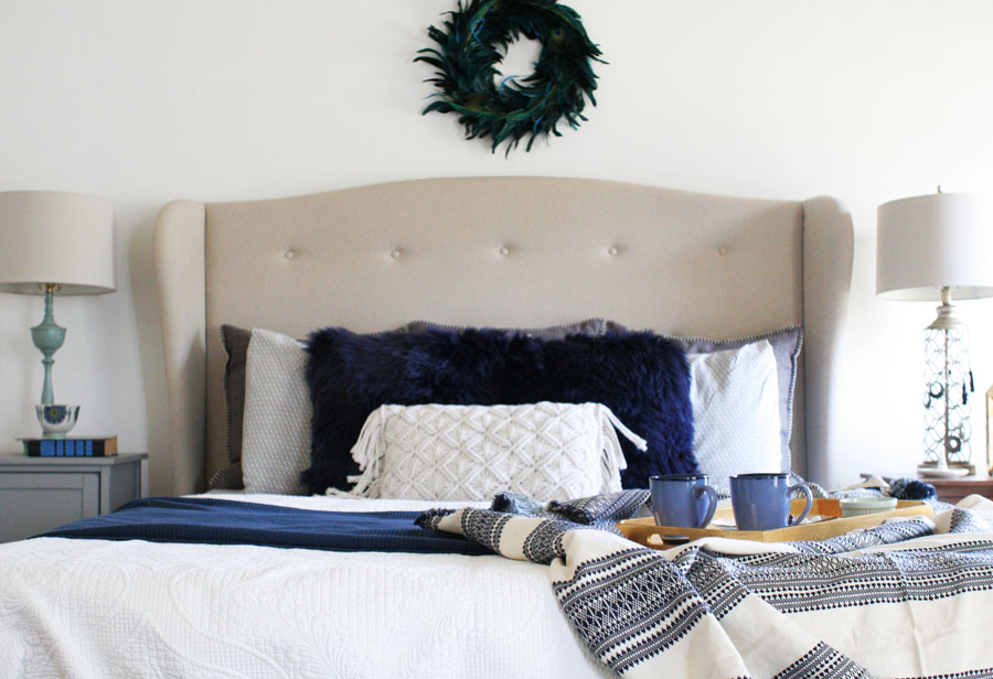 Eclectic Christmas Bedroom with Upholstered Headboard, White Quilt, Sheepskin Pillows, Crocheted Pillow, and Pom Pom Throw