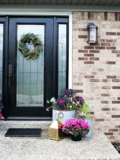 Black Front Door with Christmas Wreath and Pink Flowers in Planters.