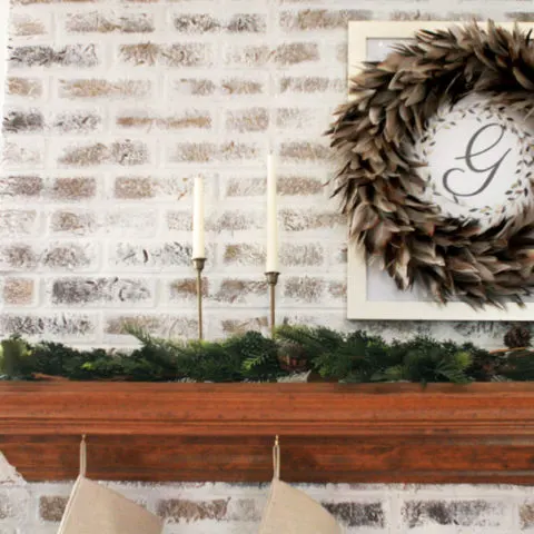 Fireplace Christmas Decorations with Feather Wreath, Brass Candles, and Garland. Christmas Mantel Ideas on a German Schmear Brick Fireplace.