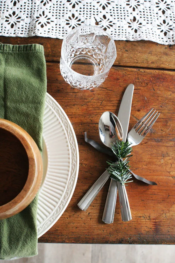 Rustic Christmas Table Place Setting with green napkins, white plates, and a christmas napkin ring