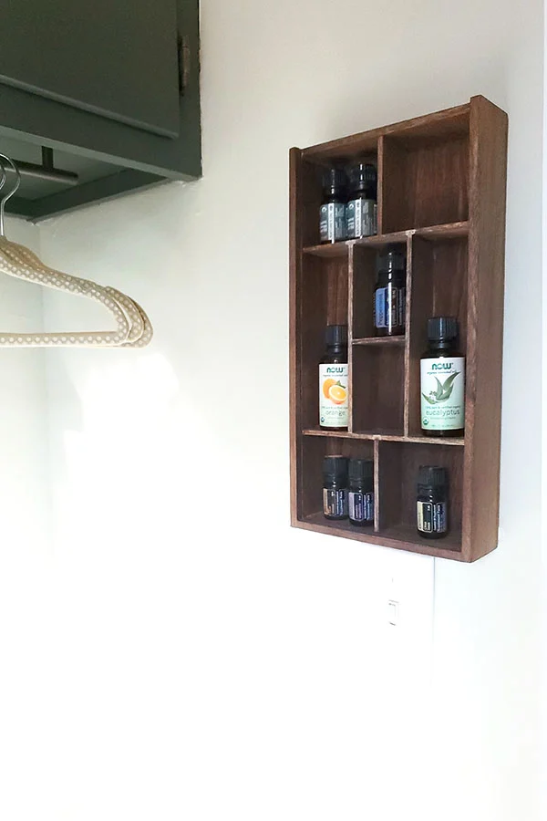Wooden DIY essential oil shelf hanging on the wall in a laundry room. 