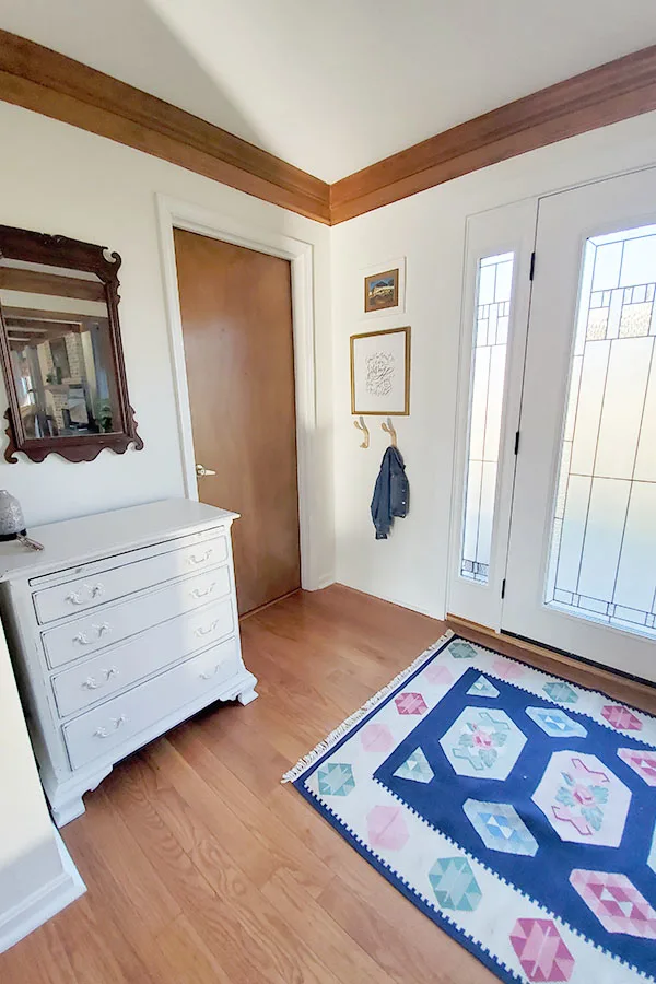 Eclectic entryway with modern coat hooks, wool Romanian rug, antique mirror, and refinished dresser