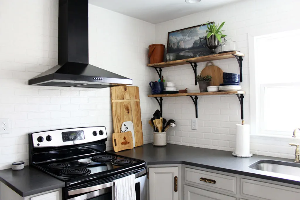 Budget kitchen remodel with gray painted cabinets, reclaimed wood shelves, and black range hood