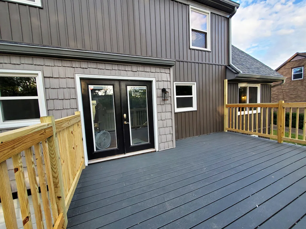 Modern cottage home exterior with board and batten siding, composite decking, and mounting posts for a shade sail