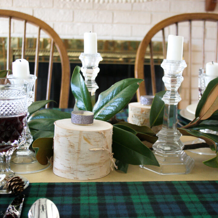 easy magnolia leaf centerpiece for Christmas from magnolia branches, blue and green plaid tablecloth, glass candle holders, birch candle holders, white candles