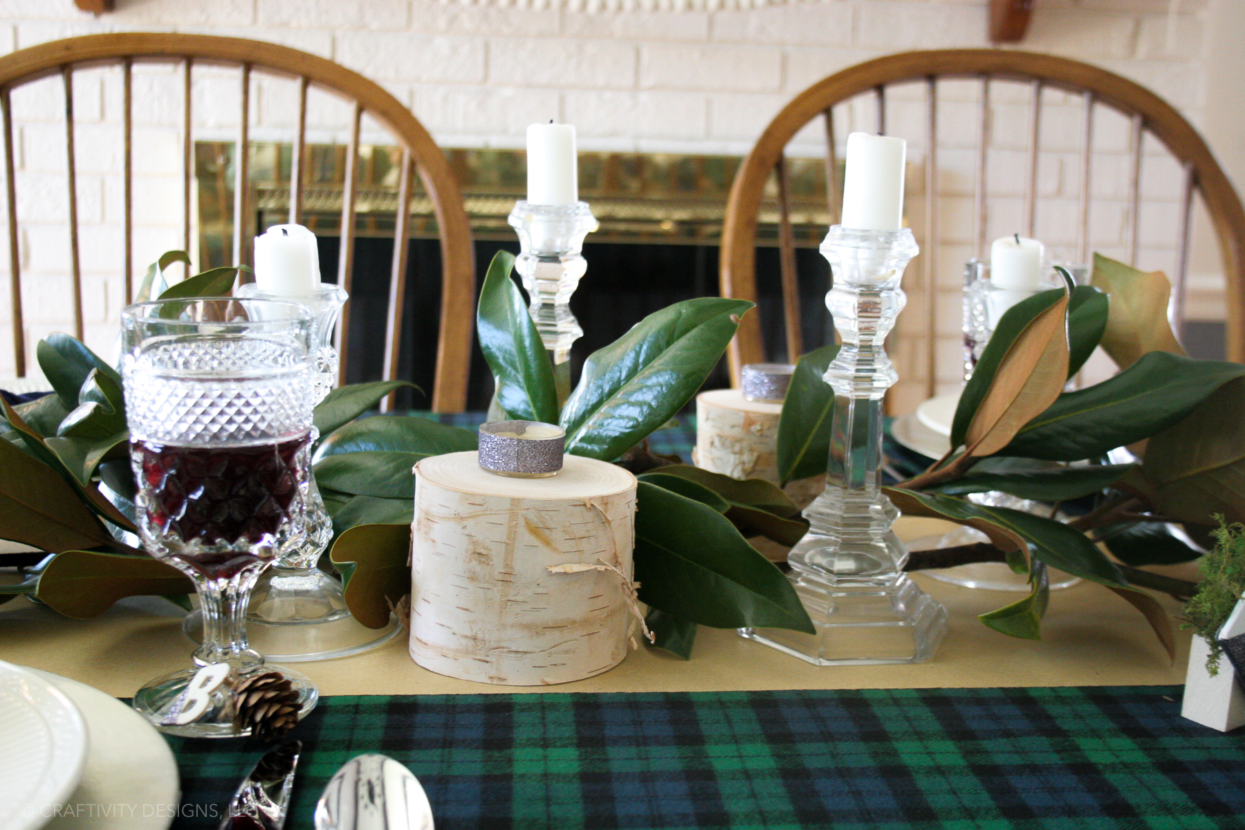 easy magnolia leaf centerpiece for Christmas from magnolia branches, blue and green plaid tablecloth, glass candle holders, birch candle holders, white candles