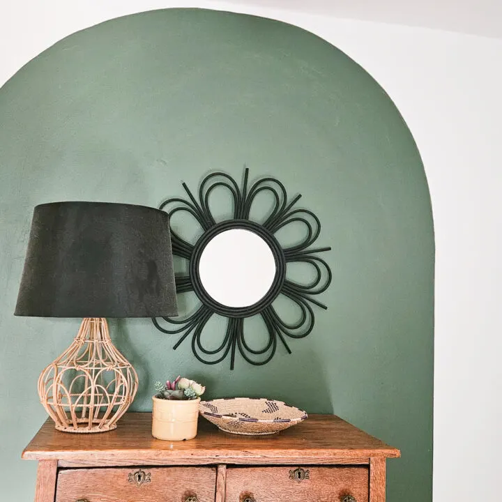 antique oak dresser in front of a dark green painted arch with a modern lamp and mirror