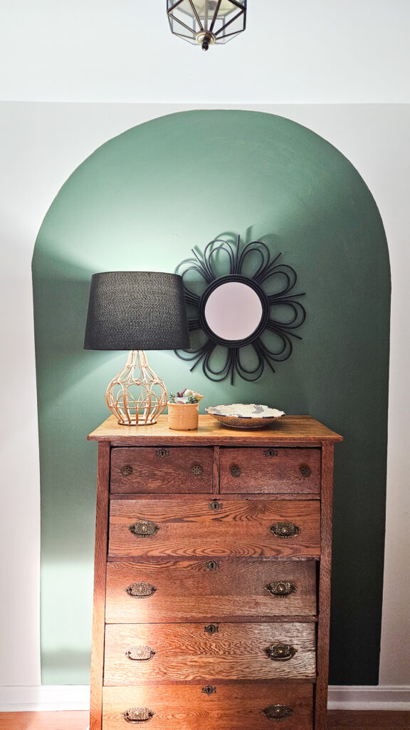 antique oak dresser in front of a dark green painted arch with a modern lamp and mirror
