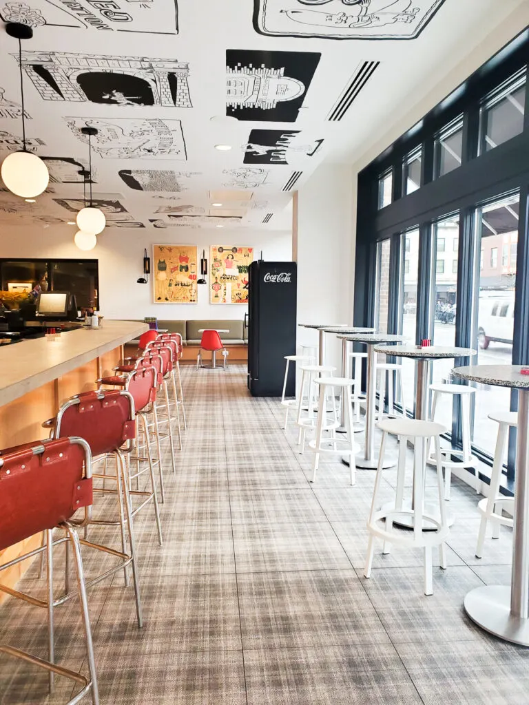 Red bar stools sit atop a plaid floor tile. While black accents paired graphic pop-art on the ceiling